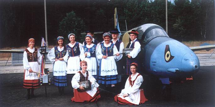 Uroczystość wręczenia sztandaru 3 Dywizjonowi Lotniczemu. Zespół wokalno-muzyczny w strojach kaszubskich obok podstawowego samolotu w Dywizjonie. 1997r.