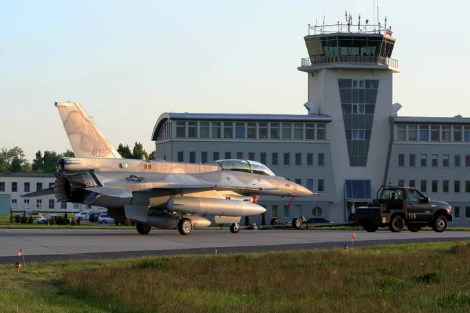 F-16 D nb 4087 na tle portu lotniczego. Samolot właśnie przybył do Rzeczypospolitej. Ma jeszcze zasłonięte Polskie znaki rozpoznawcze, a widoczne amerykańskie. Samolot jest holowany standardowym ciągnikiem. 2008r.
